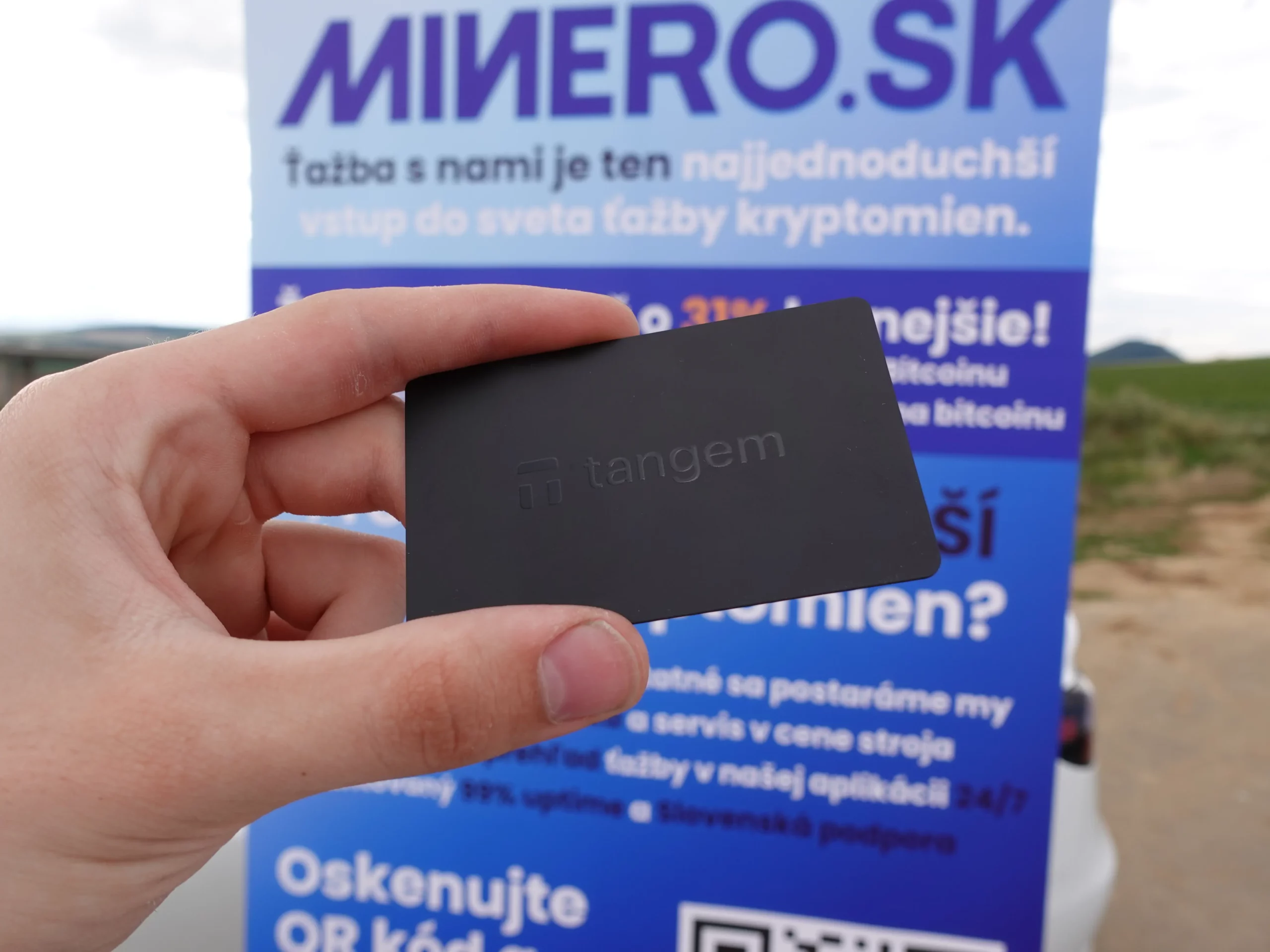 Hardvérová krypto peňaženka Tangem v ruke pred bannerom Minero.sk
