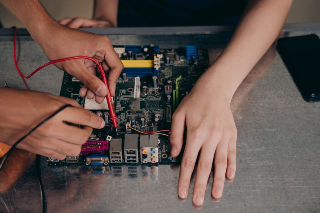 Použitý ASIC miner: na čo si dať pozor pri kúpe z bazára Ruky meria multimetrom elektronickú dosku na kovovom pracovnom stole